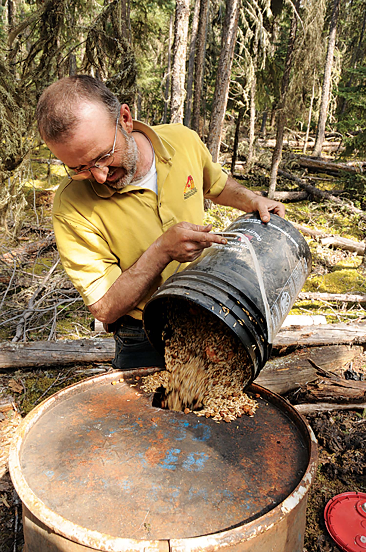man pouring food from bucket into oil drum