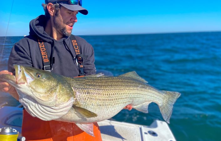 Joe Cermele with a fat striped bass standing on a boat.