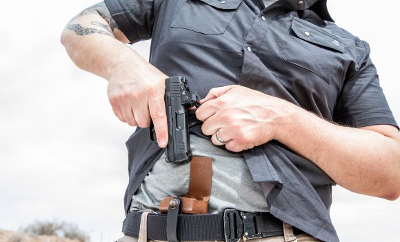 A man draws a HK CC9 pistol from concealed holster