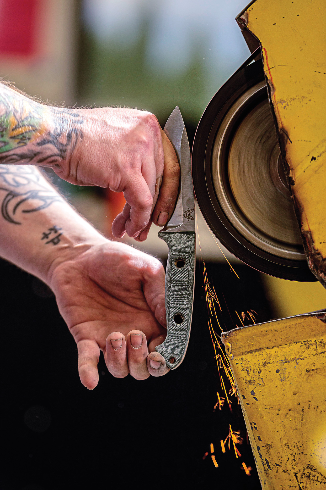 A Benchmade knifemaker grinds a knife.