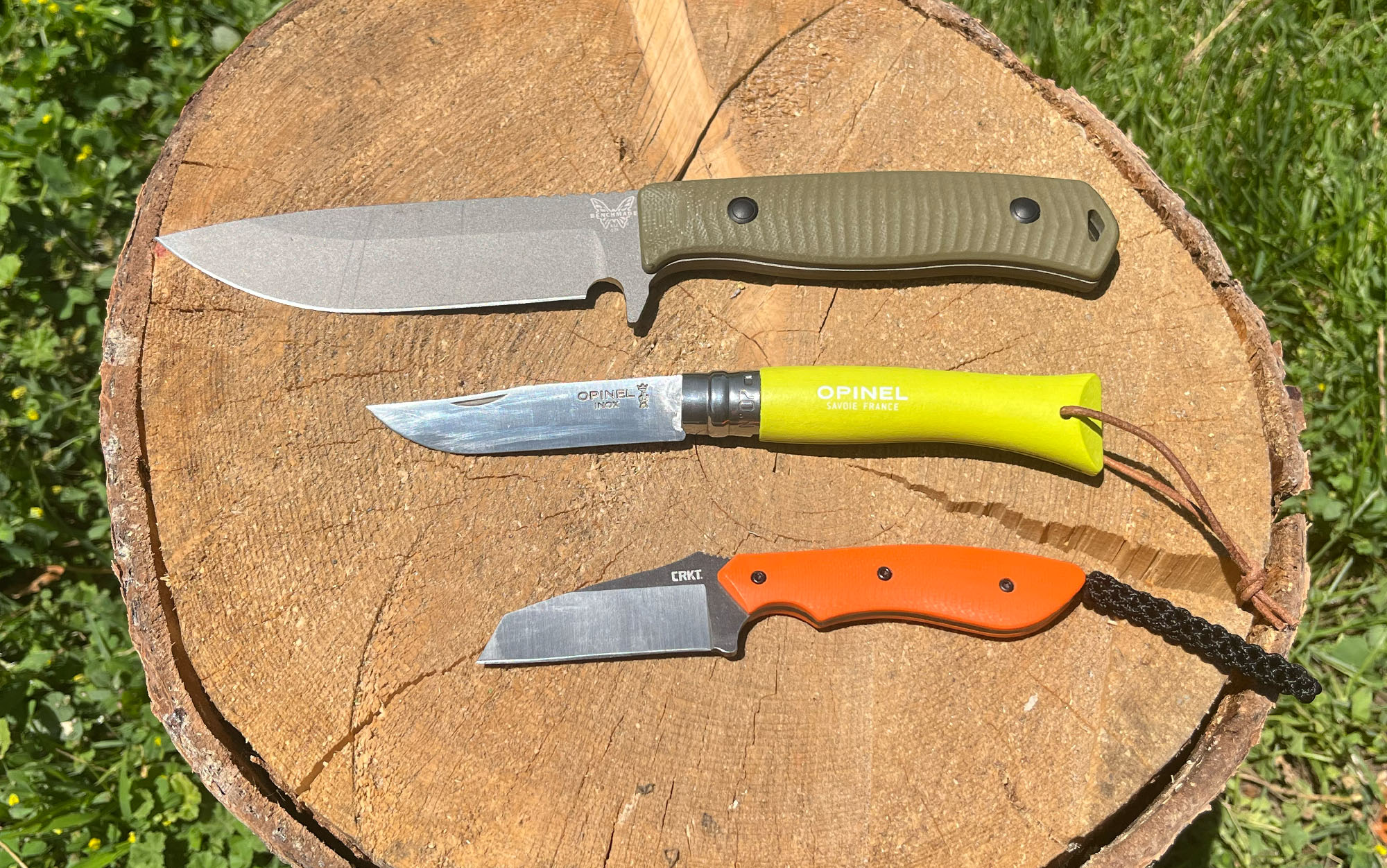 Three knives of varying blade lengths sit on a log.