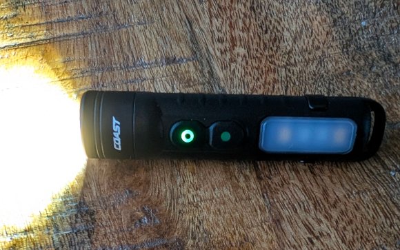 Coast mini flashlight on and sitting on a wooden table