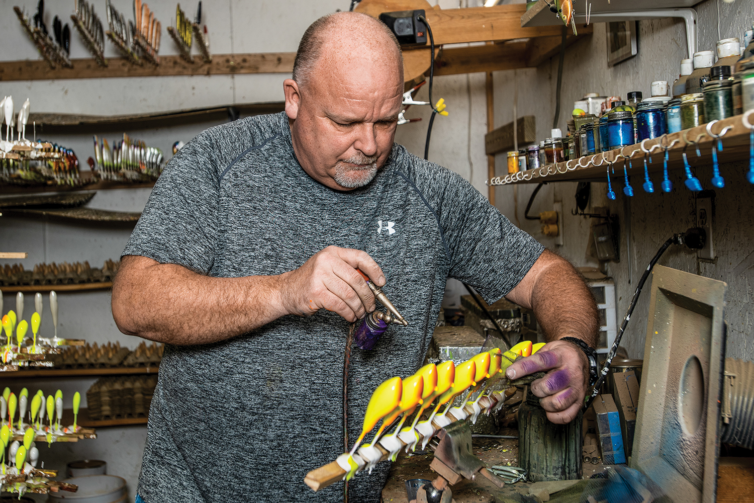 phil hunt holds a rack of crankbaits and applies paint with an airbrush
