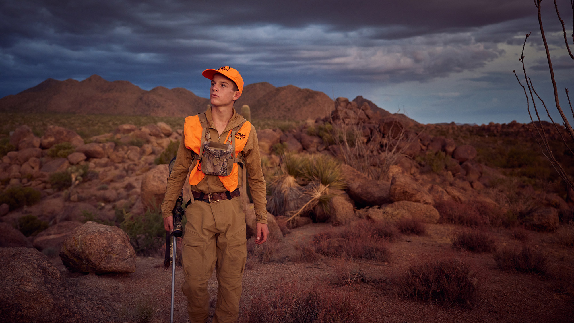 A young hunter watches for deer as he walks across the desert.