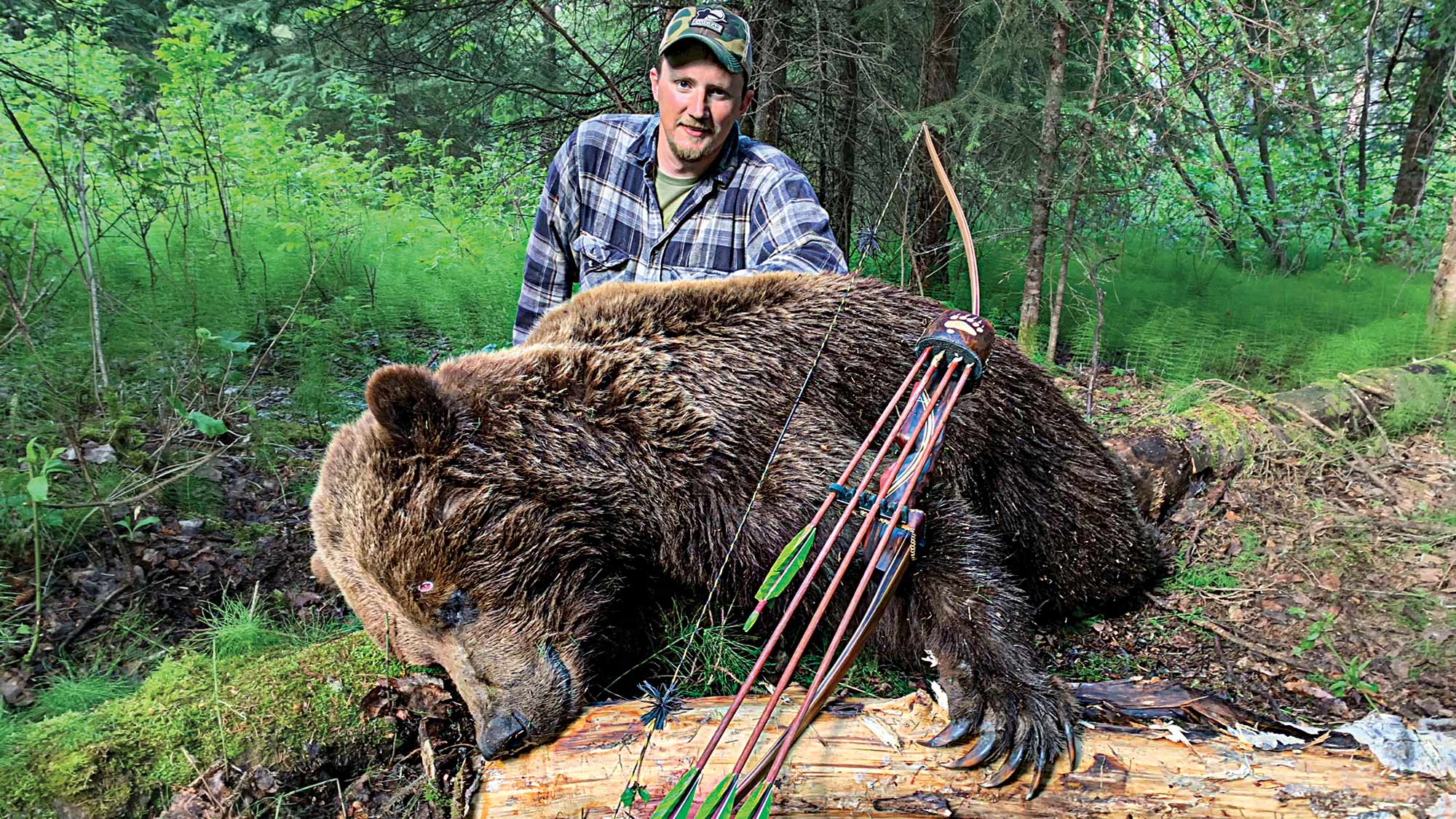 hunter poses in woods with grizzly bear and longbow and arrows