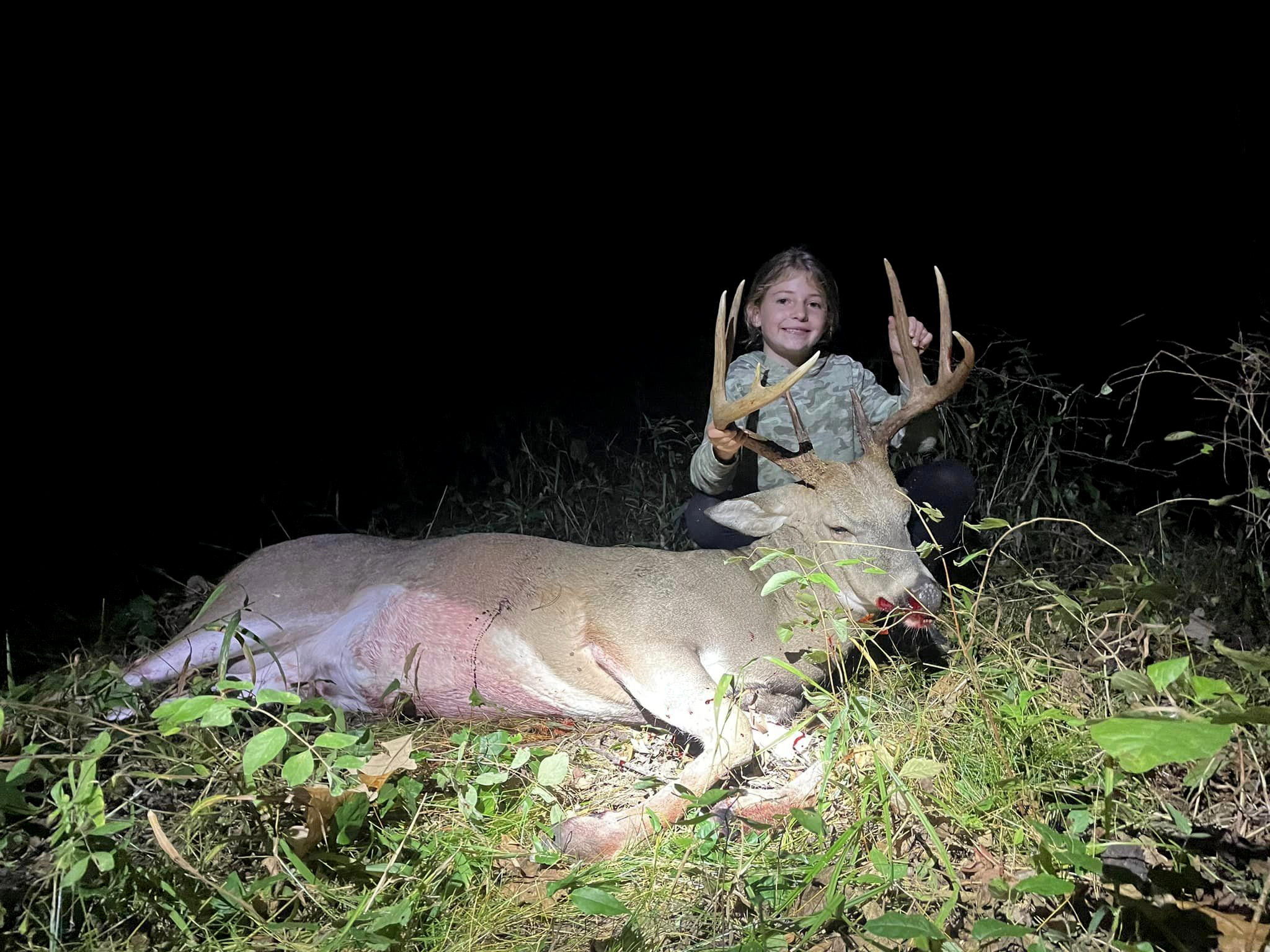 A young girl sits behind a nice buck.