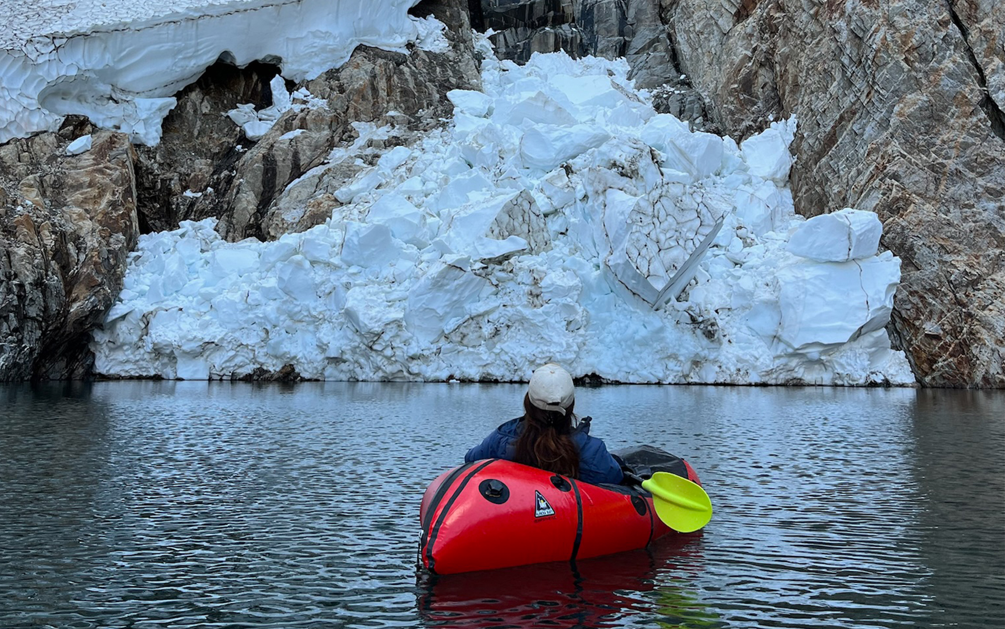 Woman paddles by glacier in Alpackaraft.