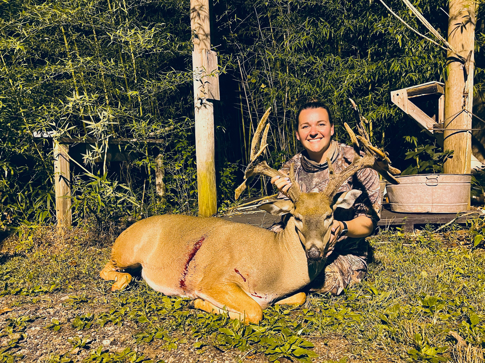 A woman sits behind a big velvet buck with three droptines and a sticker.