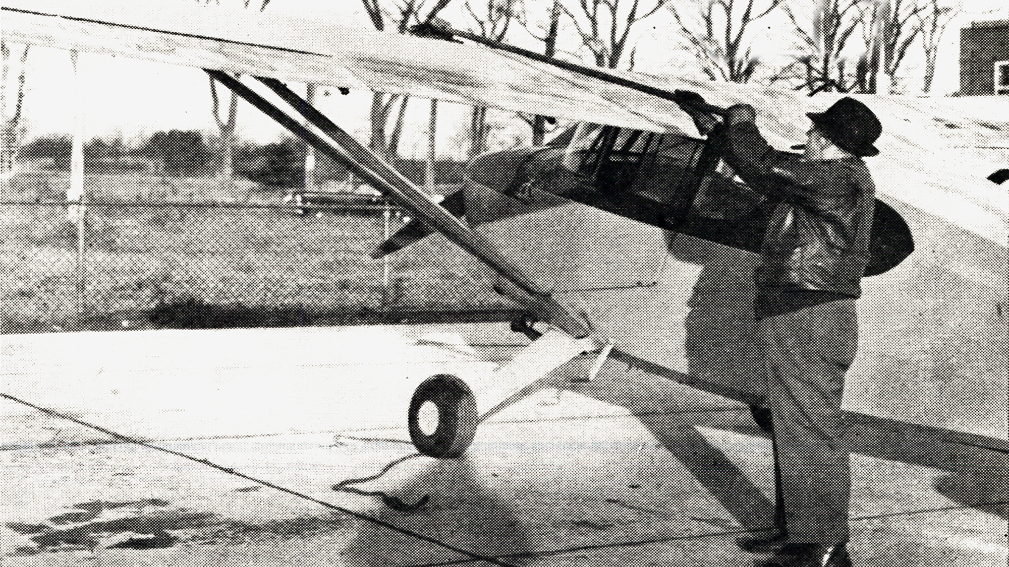man in hat and leather jacket scrapes ice off small plane's wings