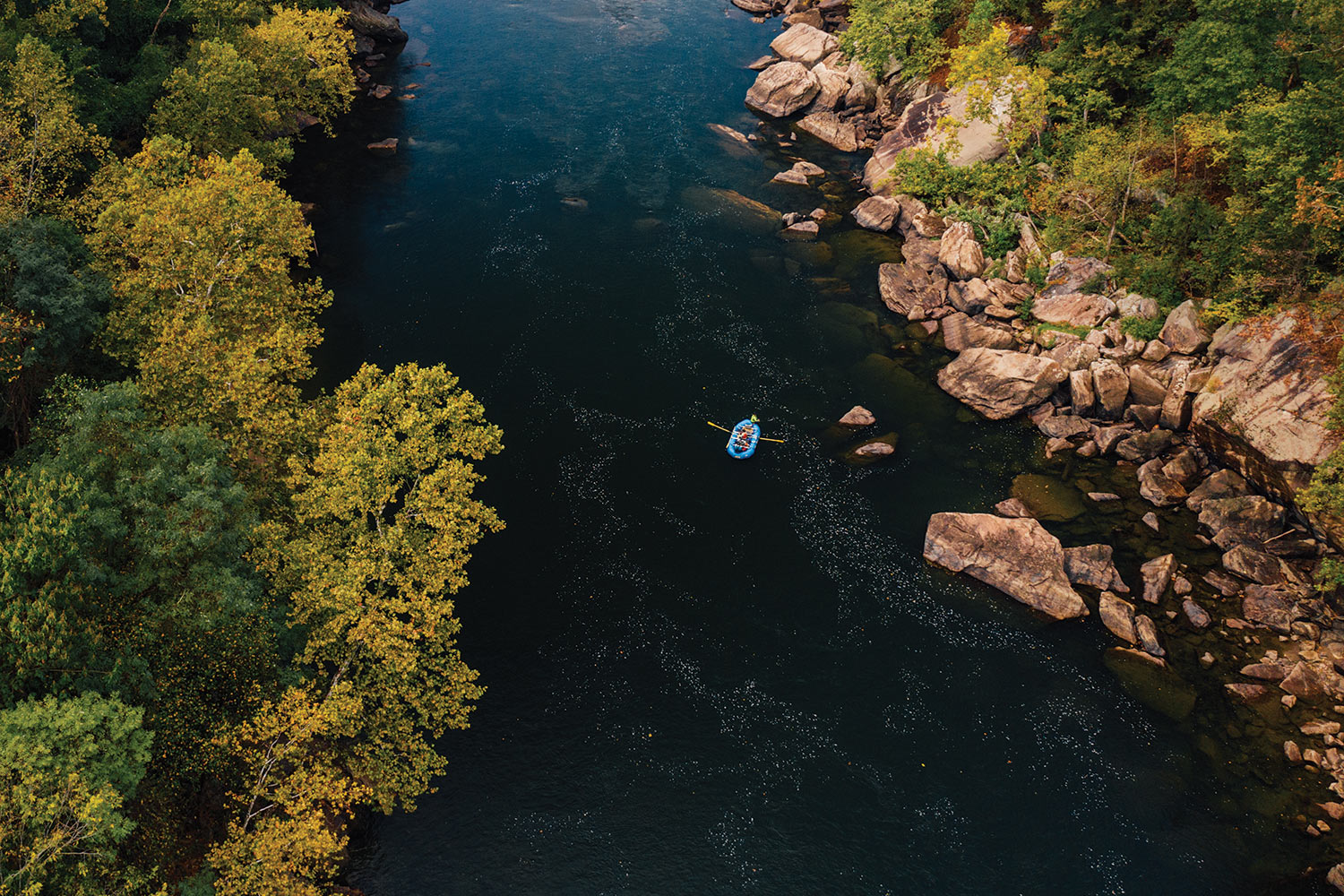 overhead view of raft moving downriver with rocks and trees on riverbank