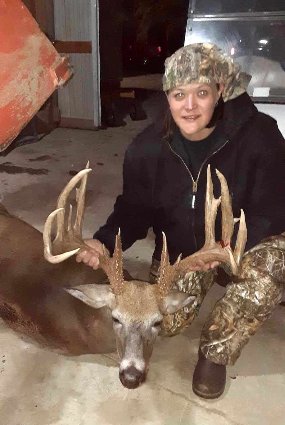 A woman holds up the antlers of a big buck on a concrete floor.