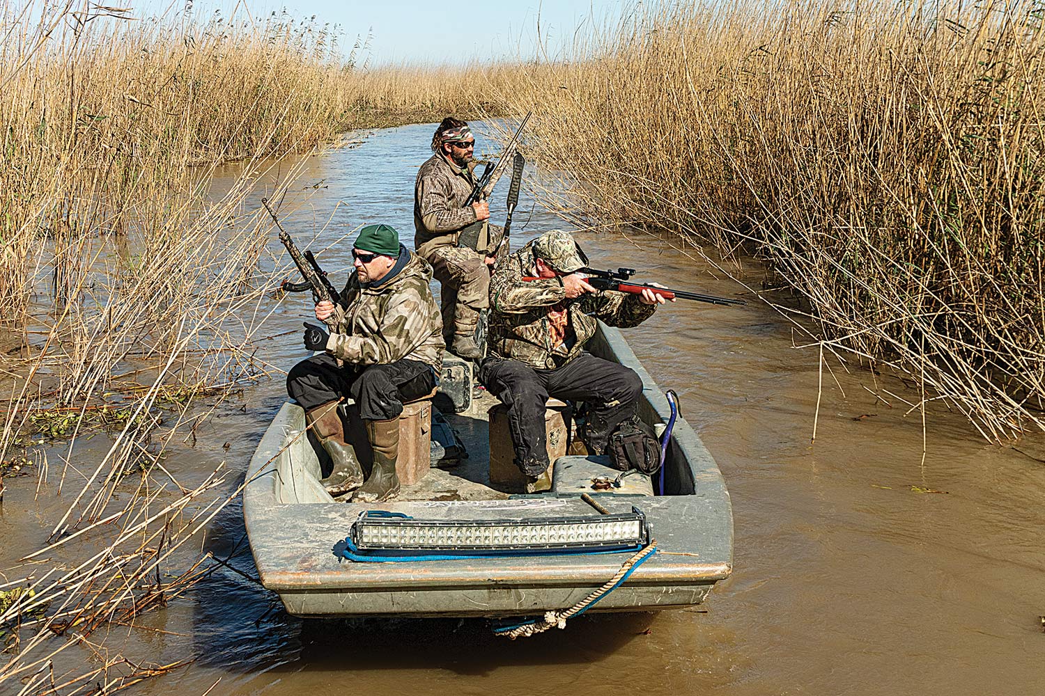 three hunters in a boat look for nutria in the brushy vegetation