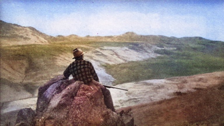 A re-colorized image of Ted Trueblood in a plaid hunting jacket looking at the mountains.