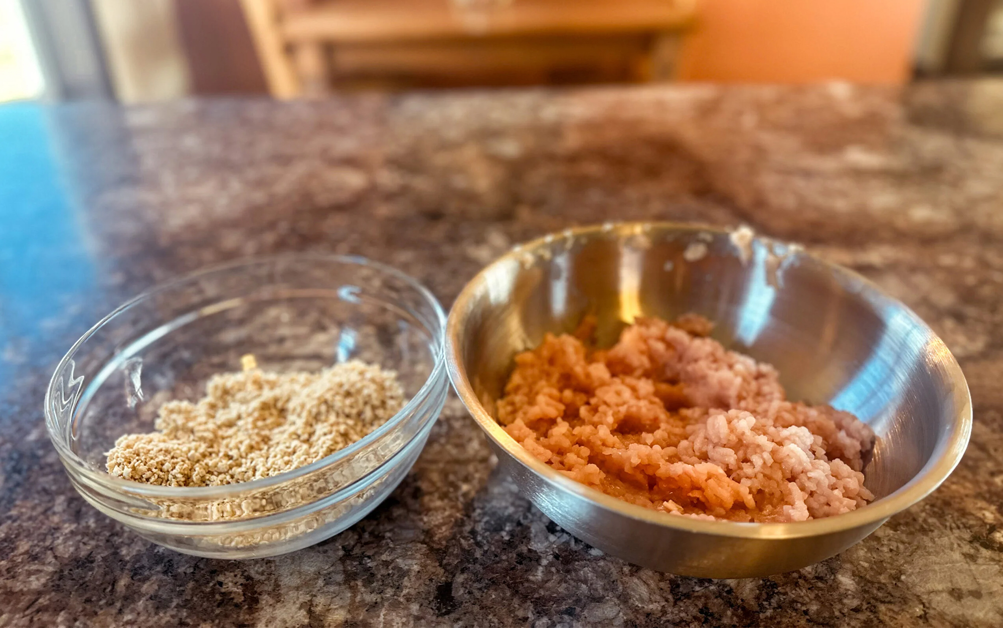 A bowl of ground meat sits next to a bowl of bread crumbs.