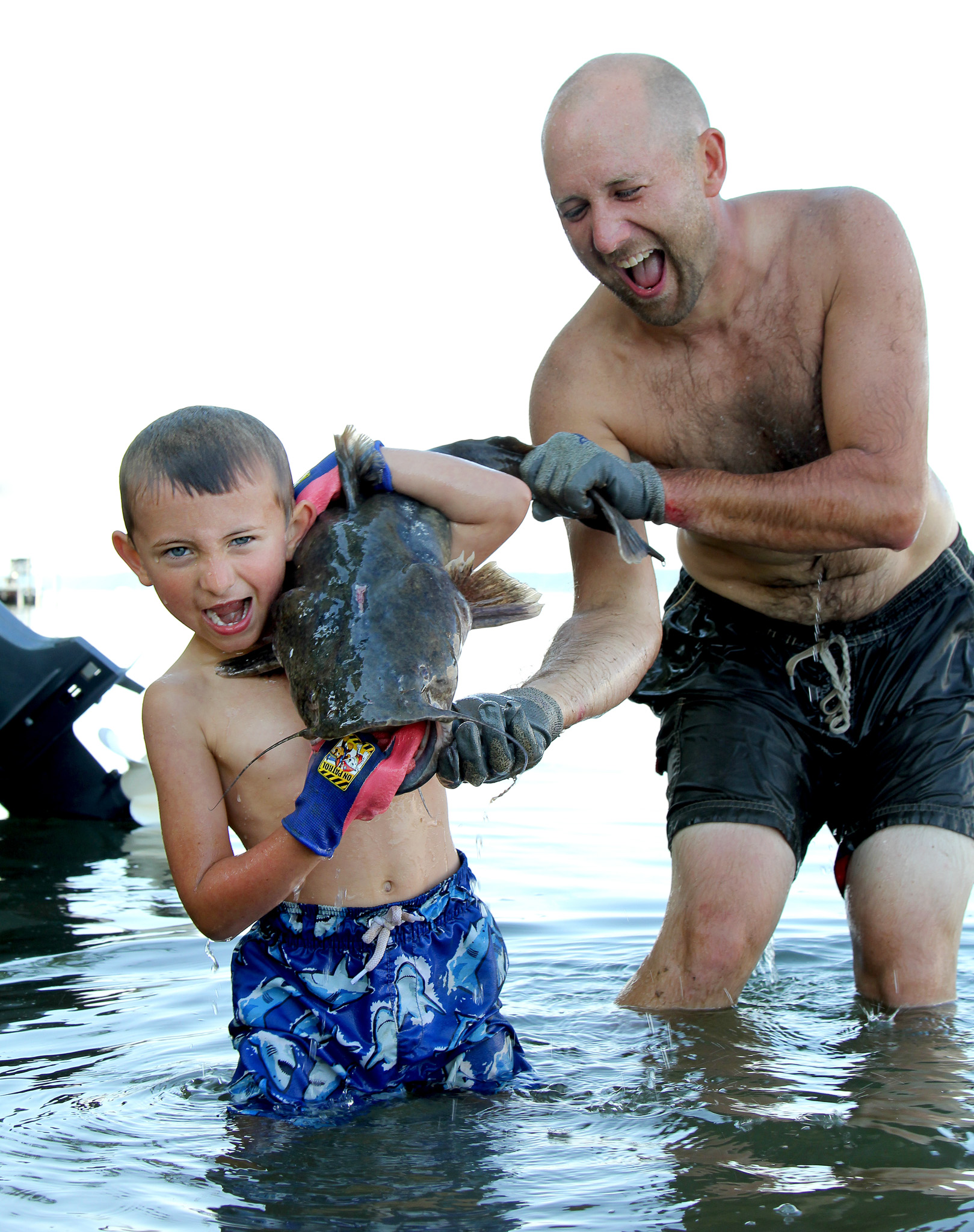 A dad helps his son hold up a flathead catfish he noodled.