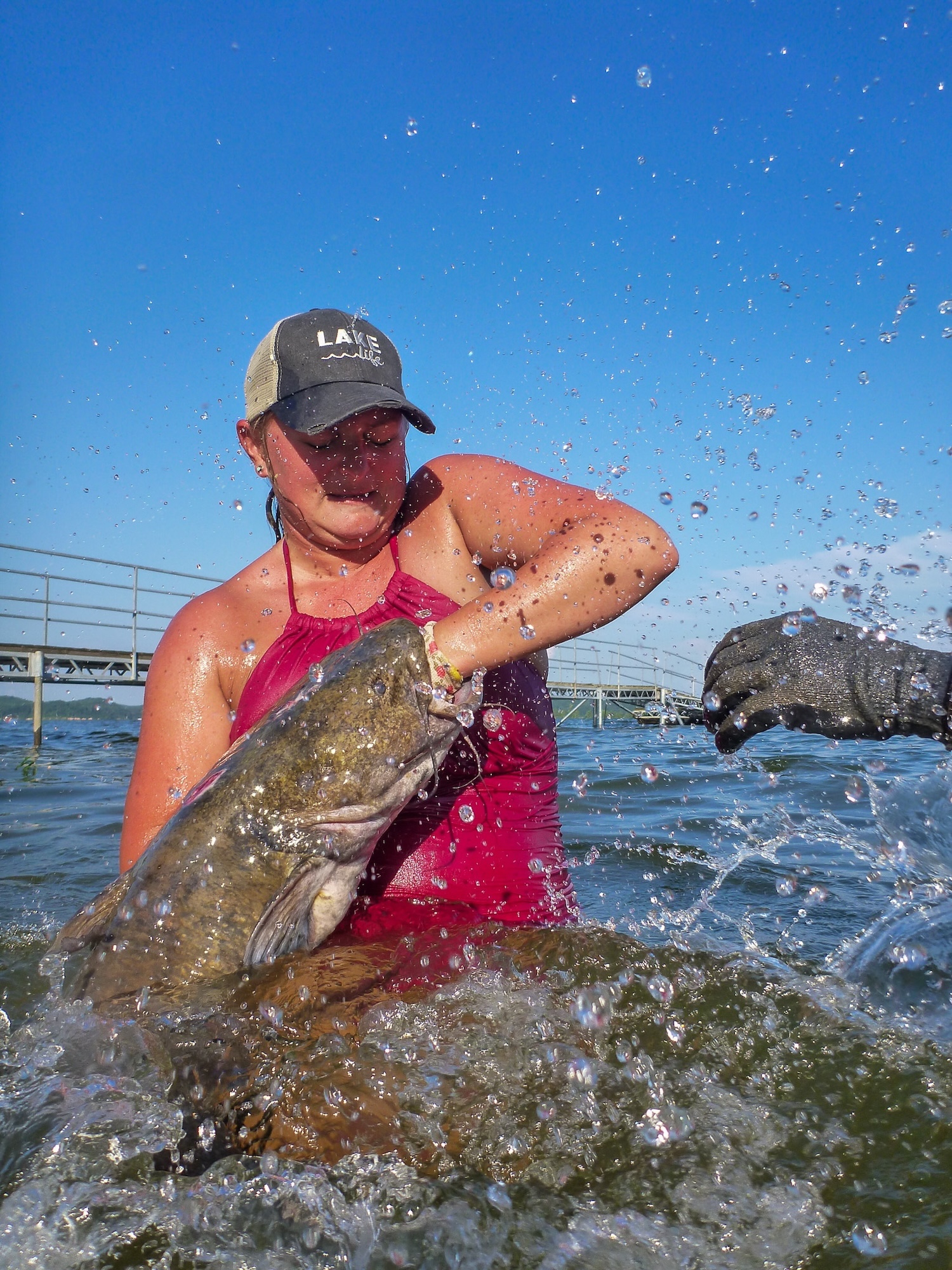 A woman in a pink swimsuit and cap grabs a flathead.