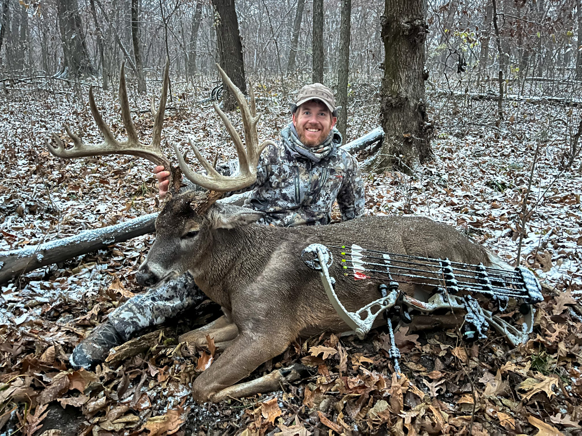 A bowhunter smiles while sitting behind a big buck in the woods.