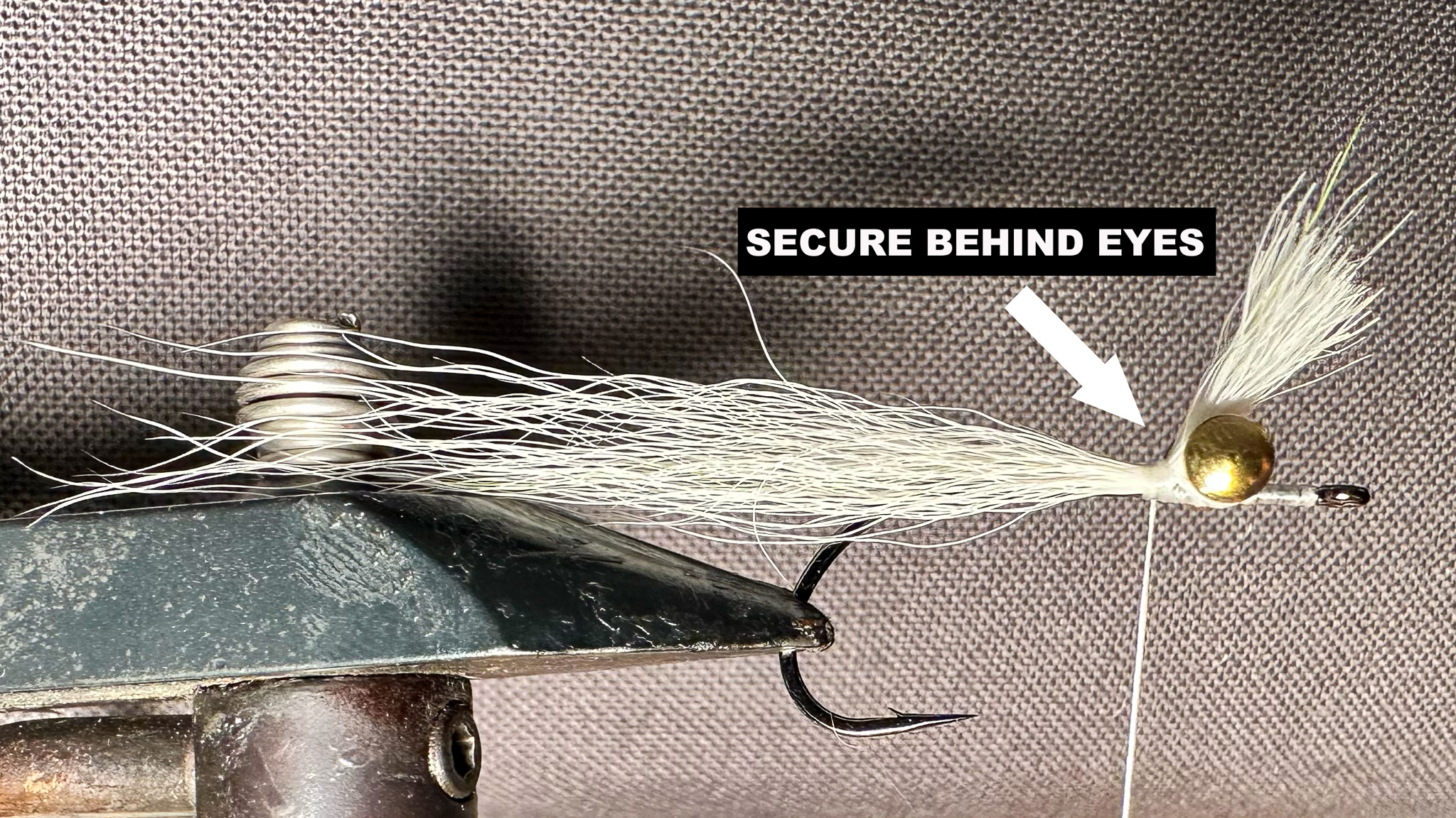 The second step of tying a Clouser, which shows an arrow pointing to how to secure the materials behind the fly's eyes.