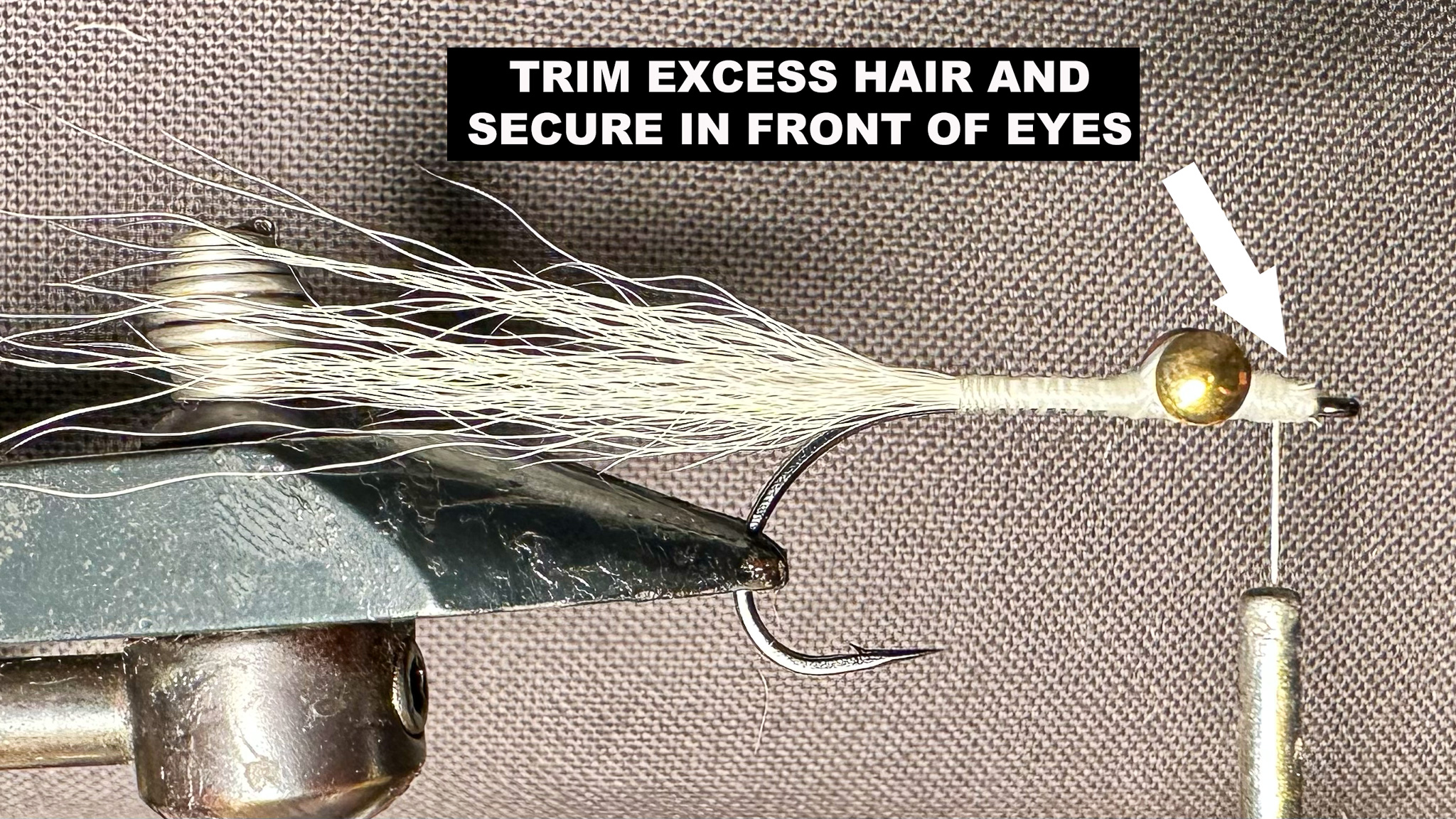 A white half-tied Clouser Minnow secured in a vise with instructions on how to secure the body thread.