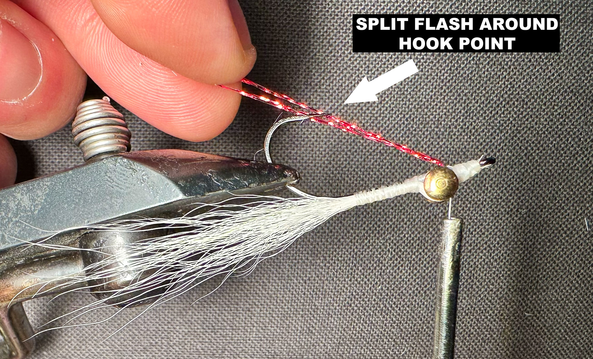 A fly in a vise with instructions and an arrow on how to split the flash around the hook point.