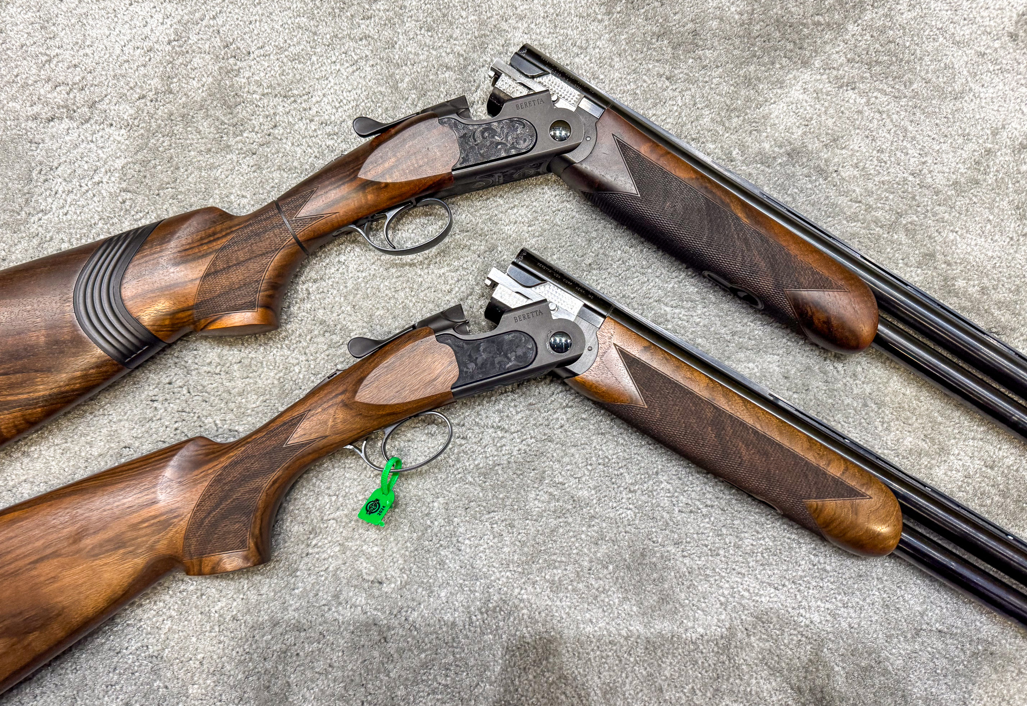 Two break-action shotguns with black receivers and dark wood, lying on a carpet.