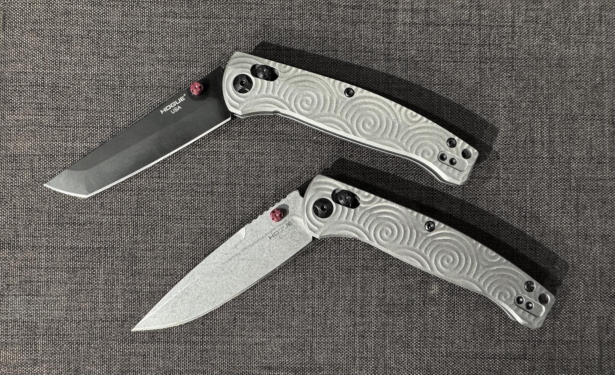 A pair of folding knives with a silver swirly handle and two different blades.