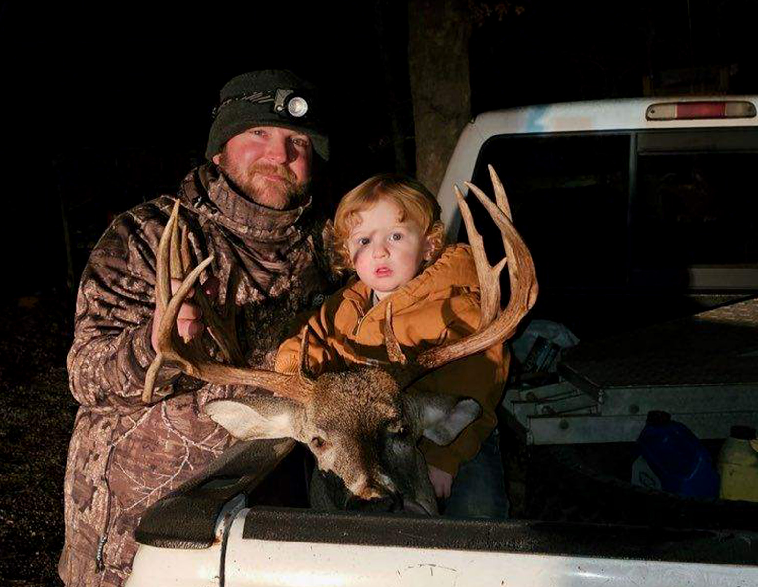 A deer hunter and his son  with a big Mississippi buck in the bed of a truck.