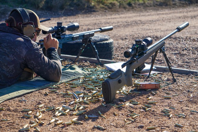 A shooter lying prone behind a rifle with a pile of brass on the ground.