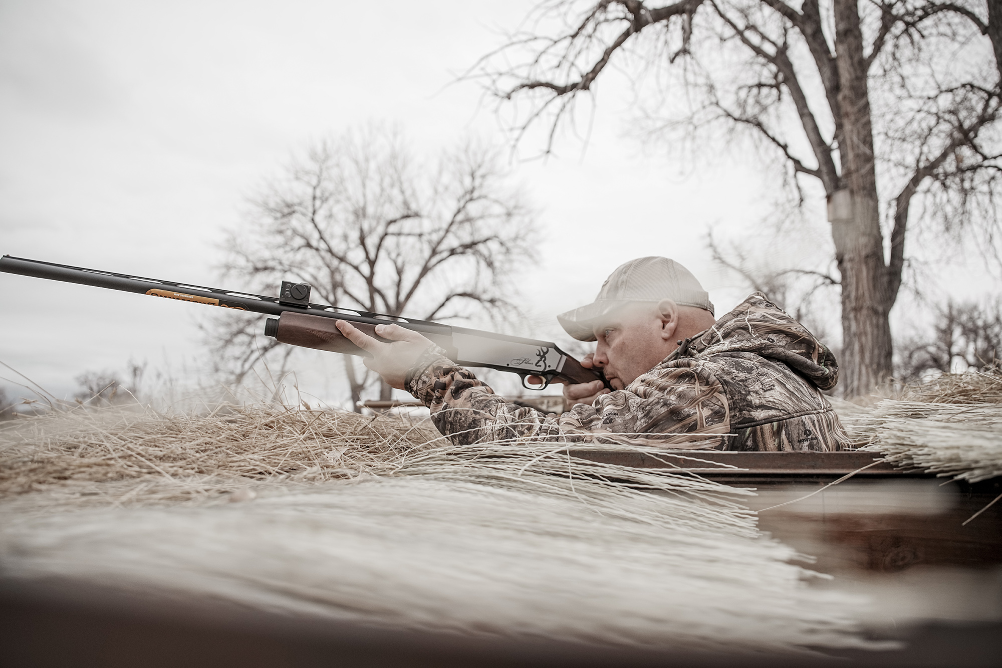 A duck hunter rises out of a blind with his shotgun shouldered and a red-dot sight mounted on the rib.