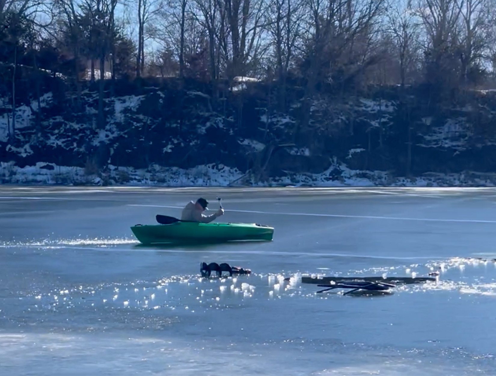 An ice fisherman scoots across the lake in a kayak.