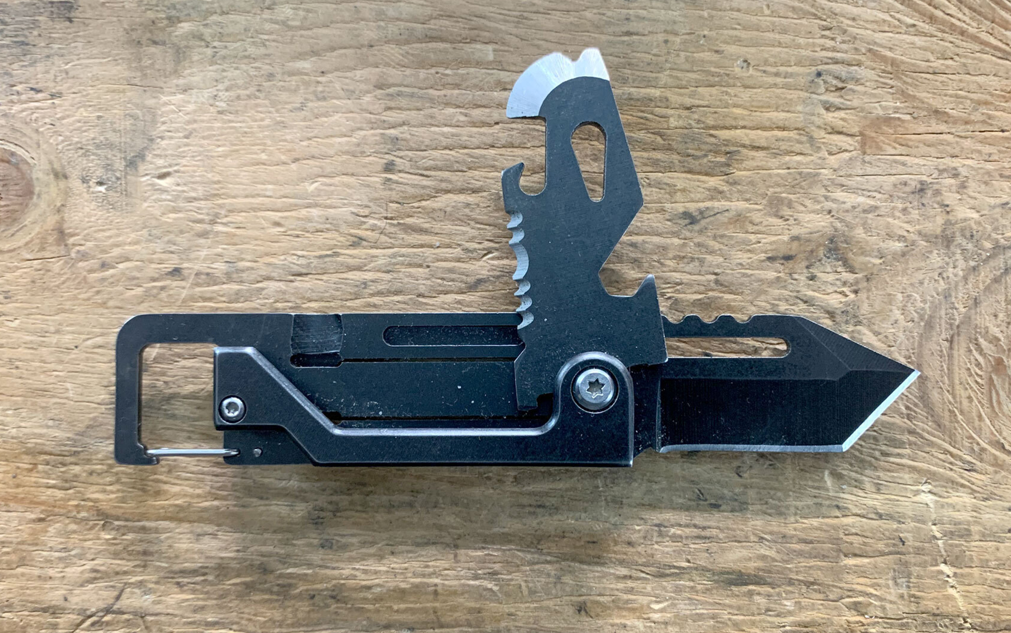 The Edcfans Keychain Multi Tool features a short, tanto-style blade, chisel/pry tip, can opener, small serrated sawing section, ¼-inch wrench, and bottle opener.