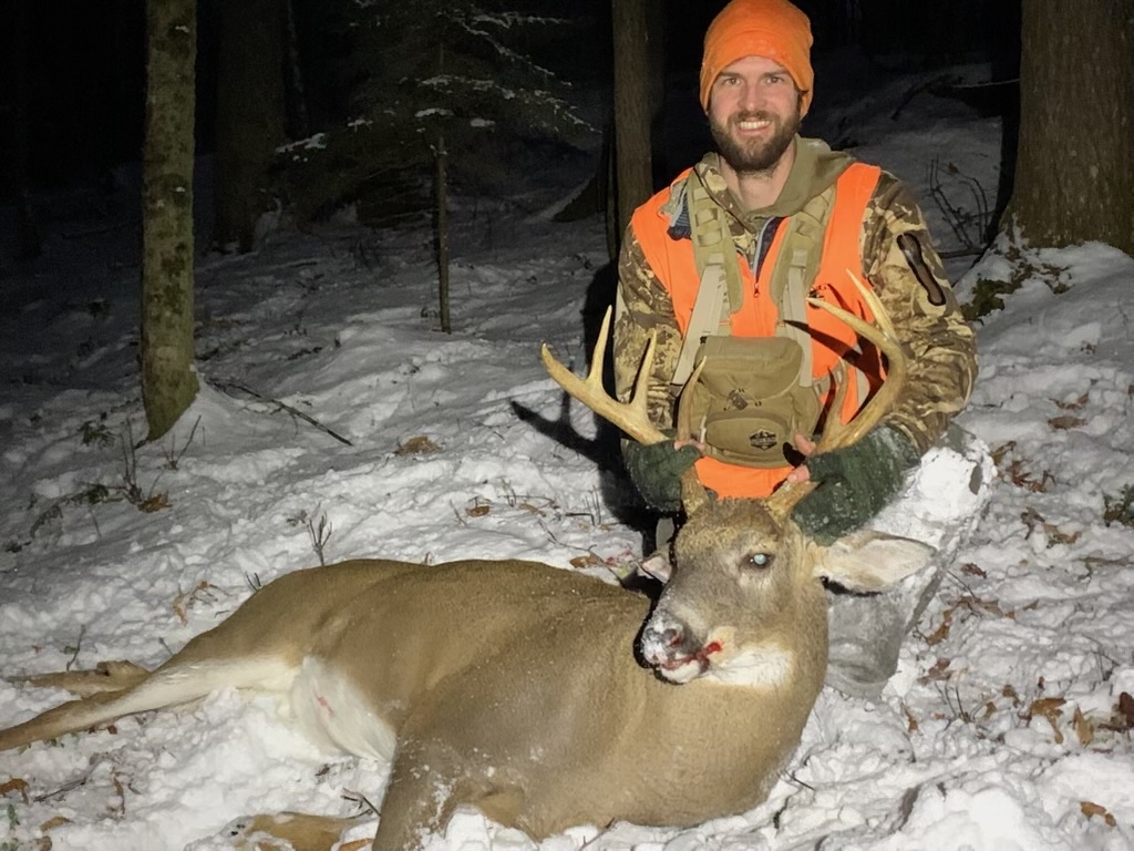 A Vermont hunter wearing orange sits behind a nice buck he tagged.