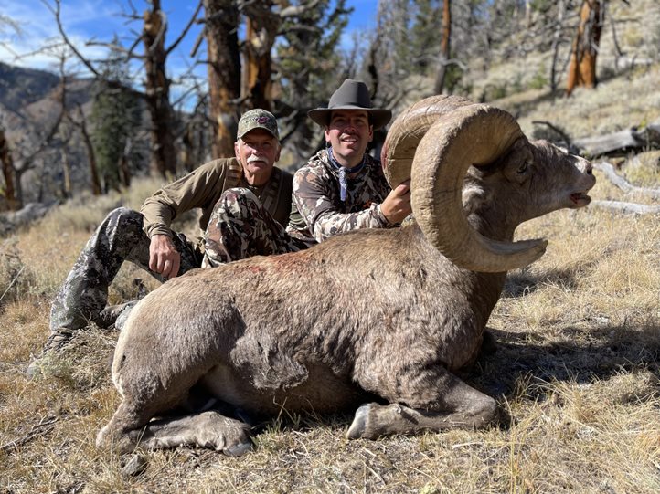 A hunter sits behind a bighorn ram with his buddy.