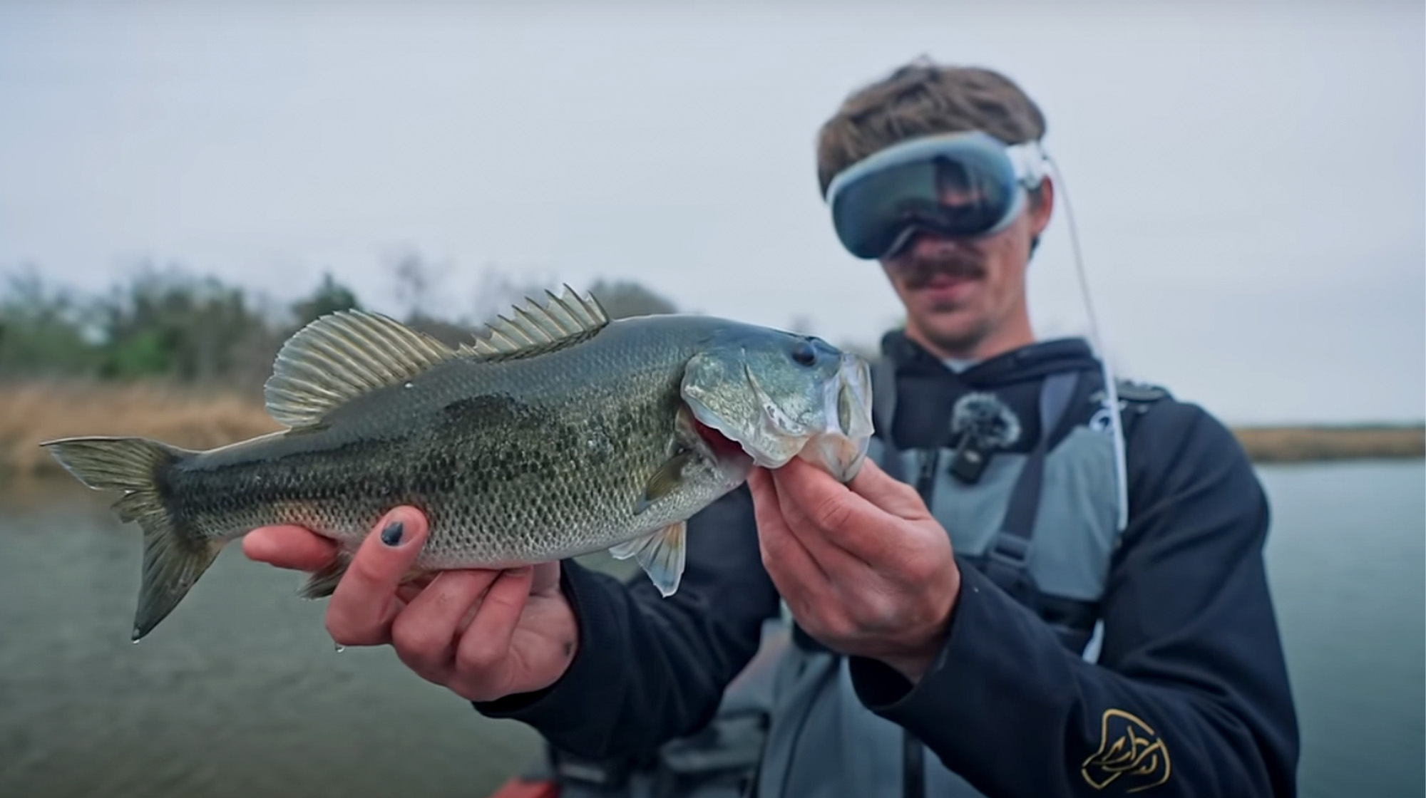 A fisherman wearing 3D goggles holds up a bass.
