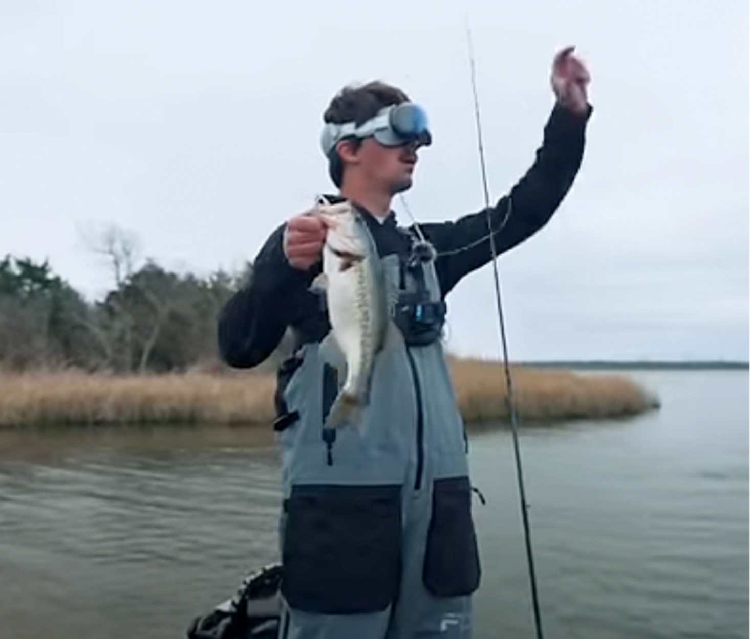 An angler holds up a bass while wearing a pair of Apple Vision Pro goggles.