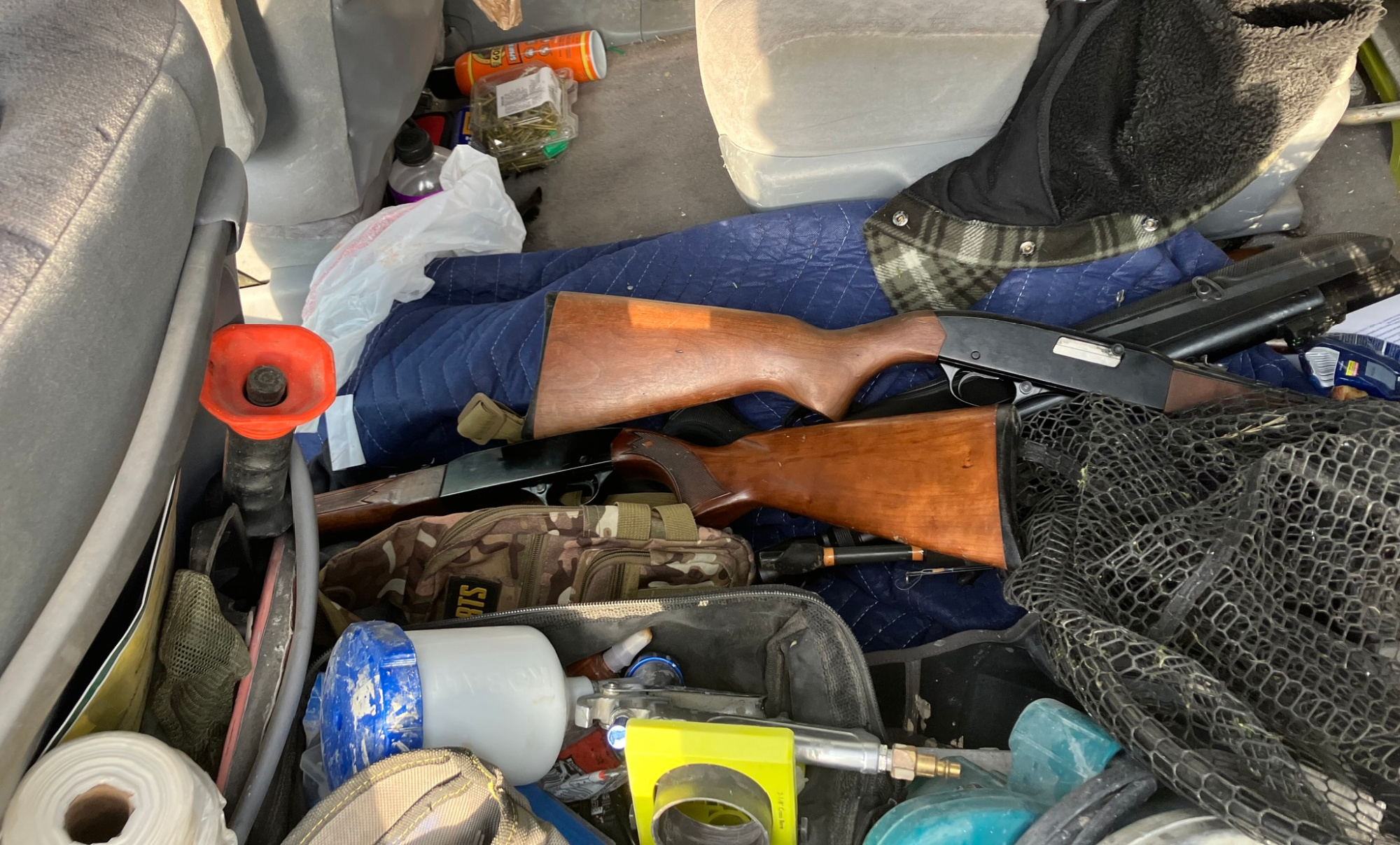 A pile of tools and guns inside a messy vehicle.