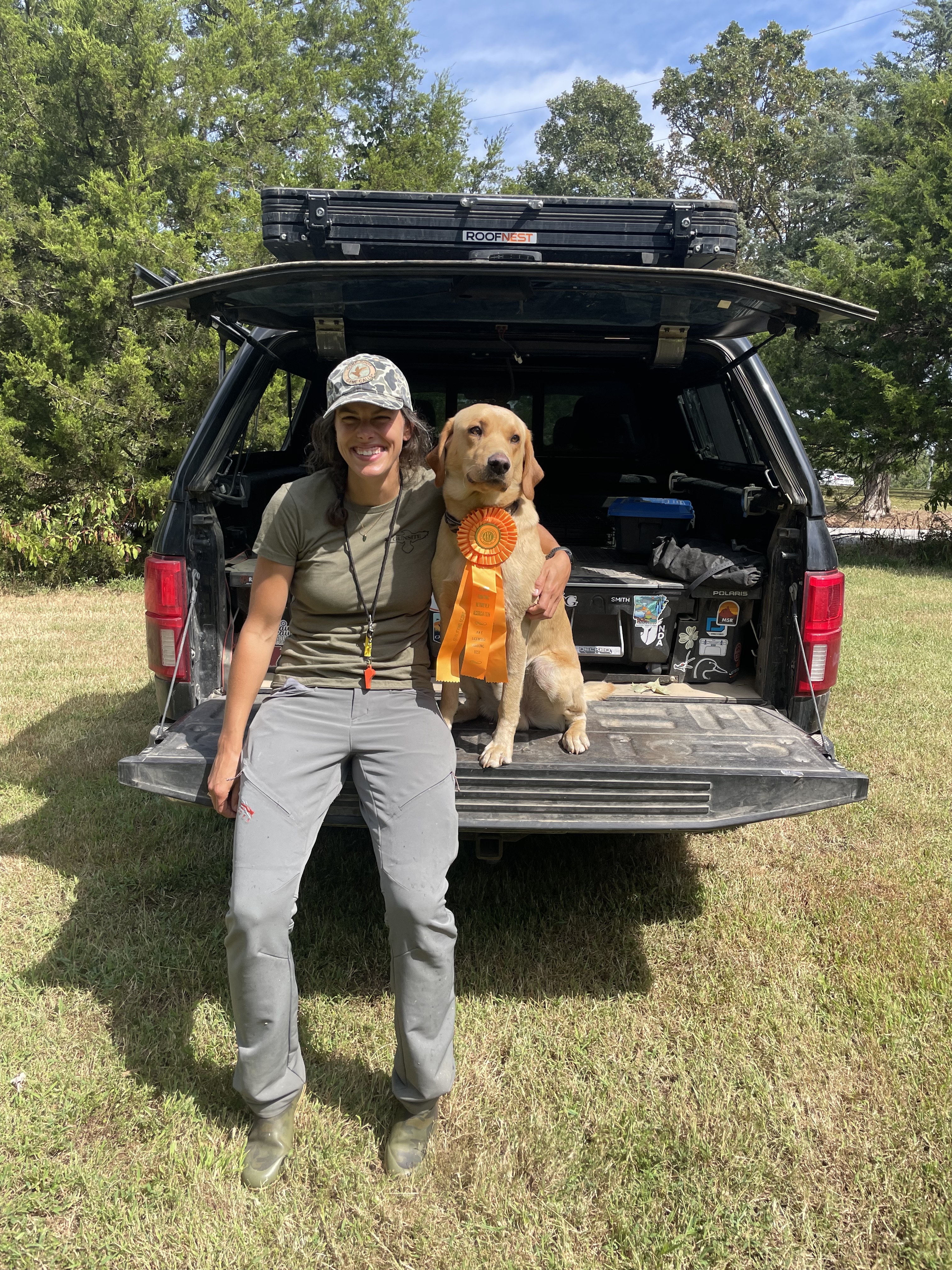 A woman with her Lab wearing a yellow ribbon for a hunt test.