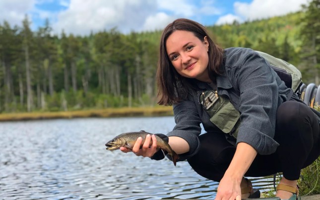 Woman holds trout over stream.