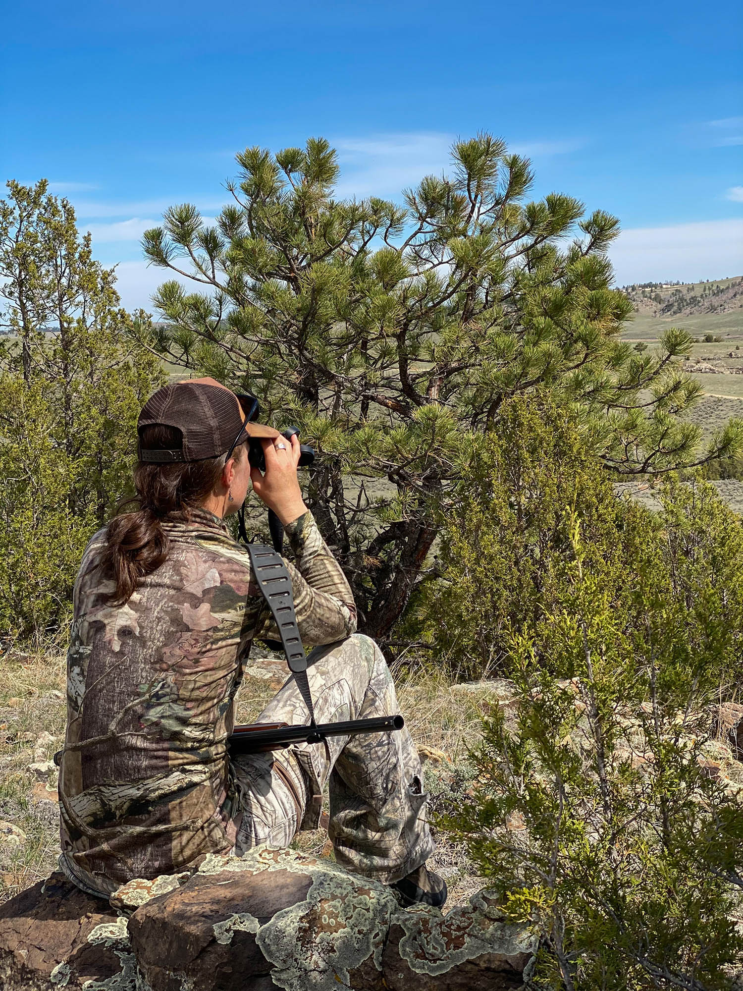A Western turkey hunter sits in a clearing and glasses for birds.