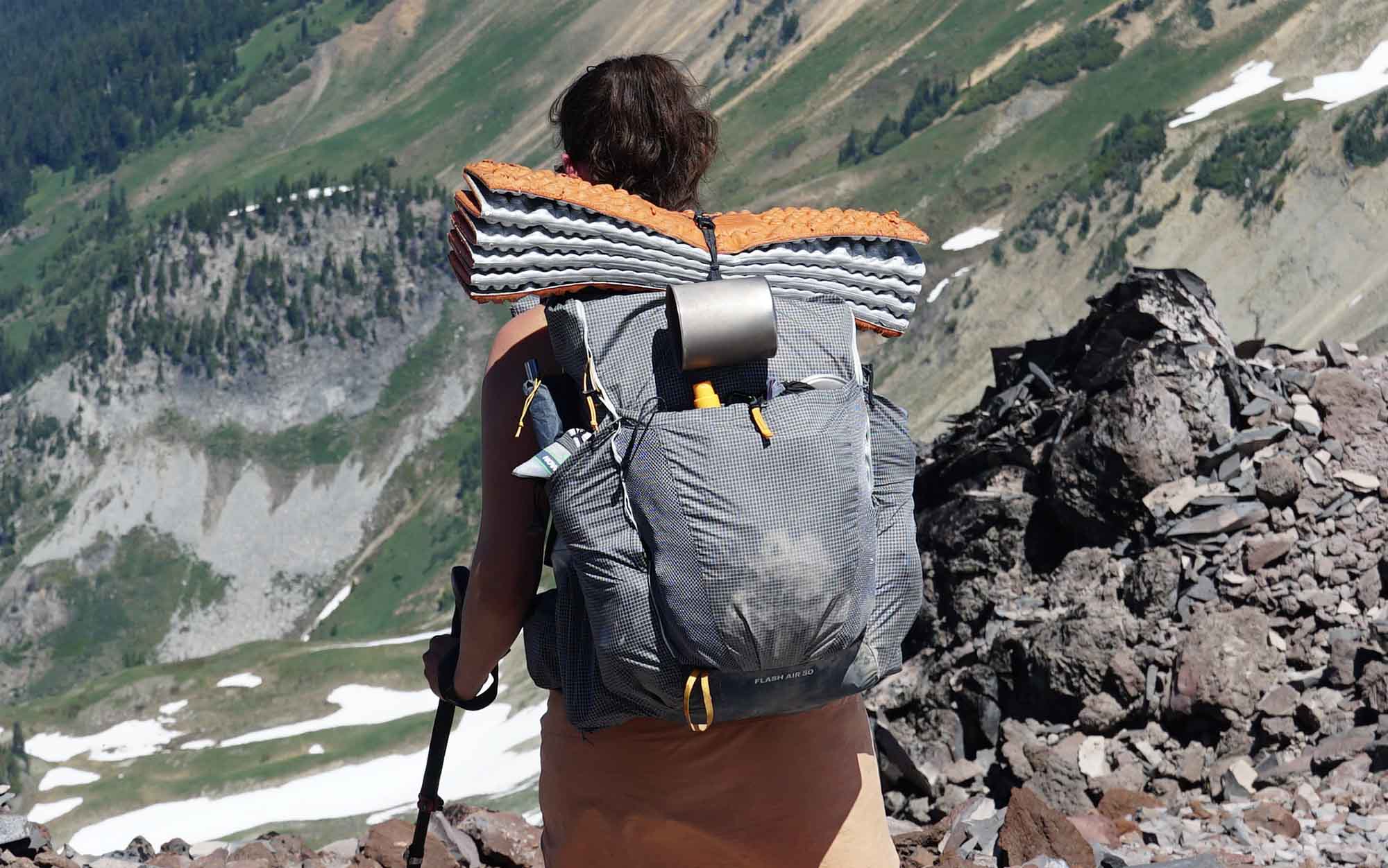 woman walking down a mountain ridge wearing the REI Flash Air 50 backpack