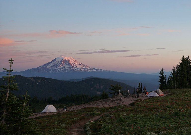three tents on an alpine ridge with a volcano in the background at sunset