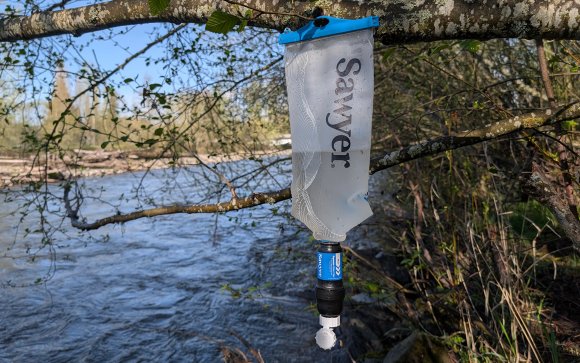 Sawyer Squeeze with squeeze bag hanging from a tree branch with a river in the background