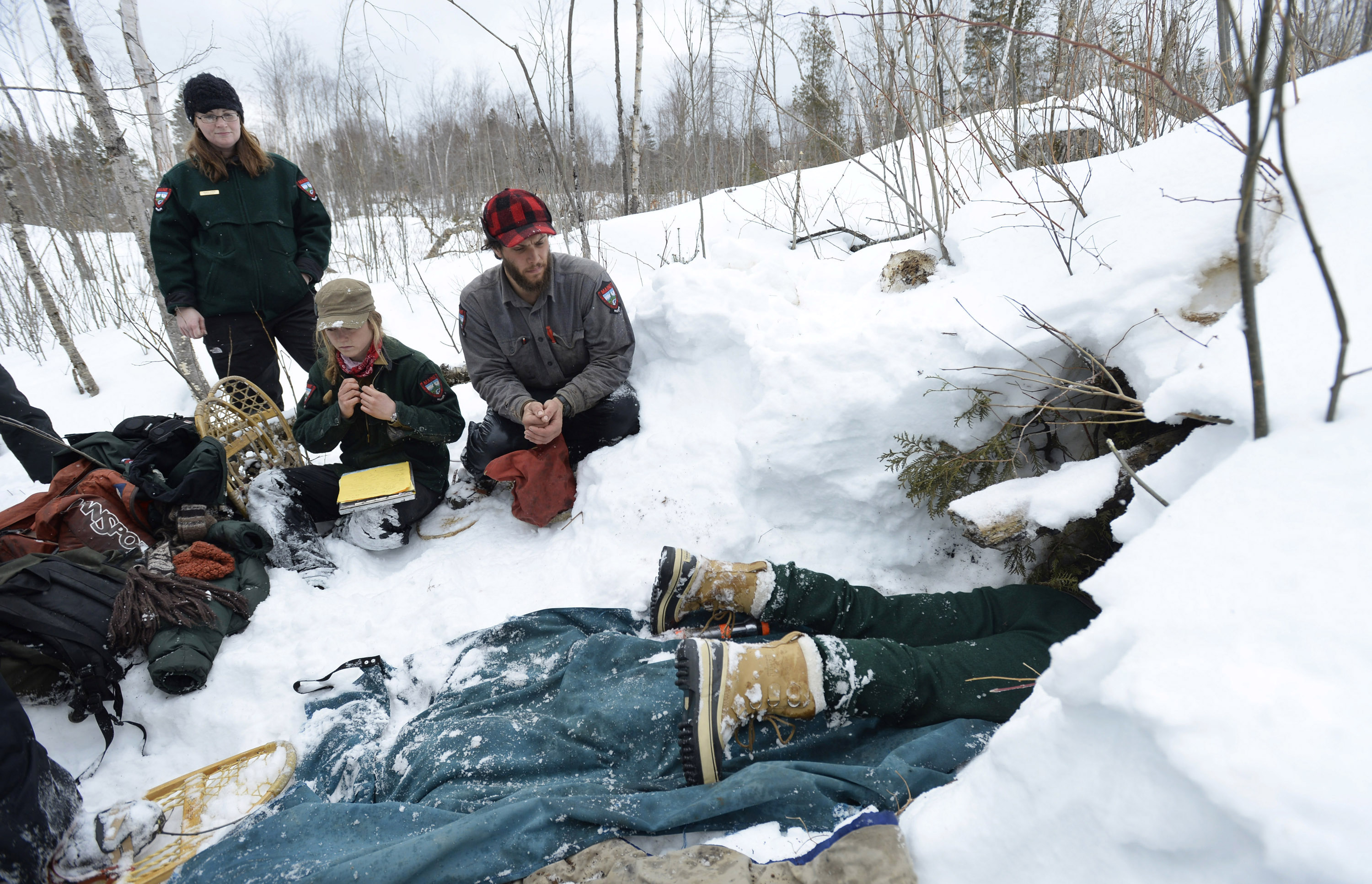 A photo of biologists surrounding a snowy bear den in Maine.