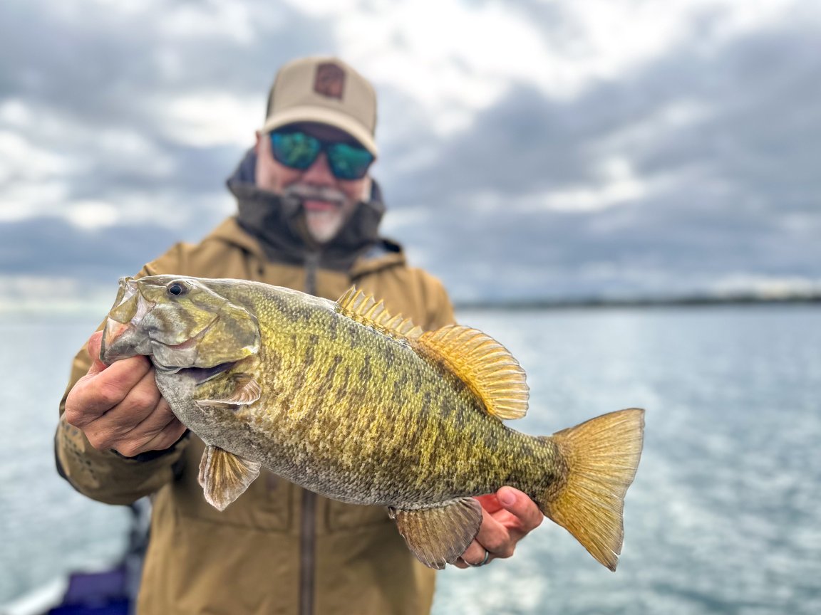 A man holds up a nice smallmouth bass caught in the fall.