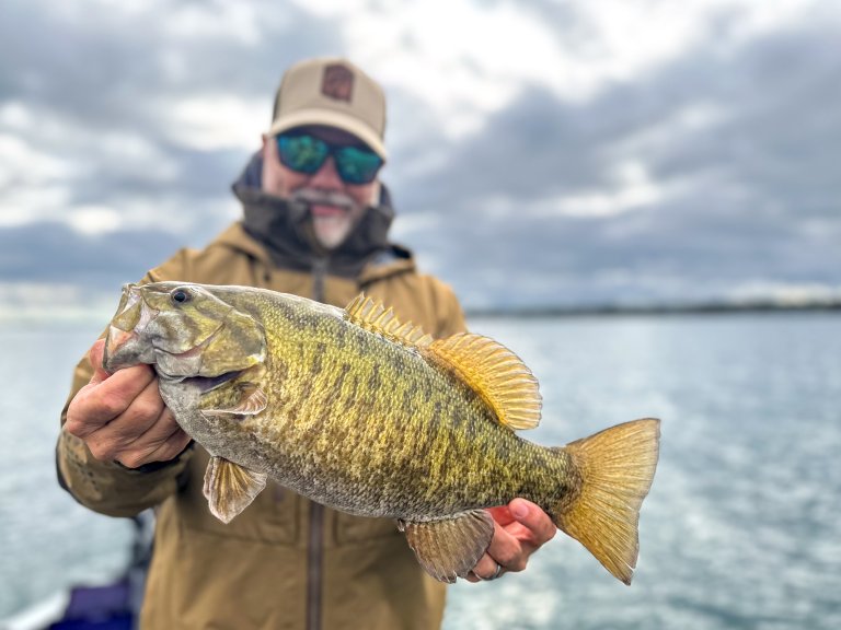 A man holds up a nice smallmouth bass caught in the fall.