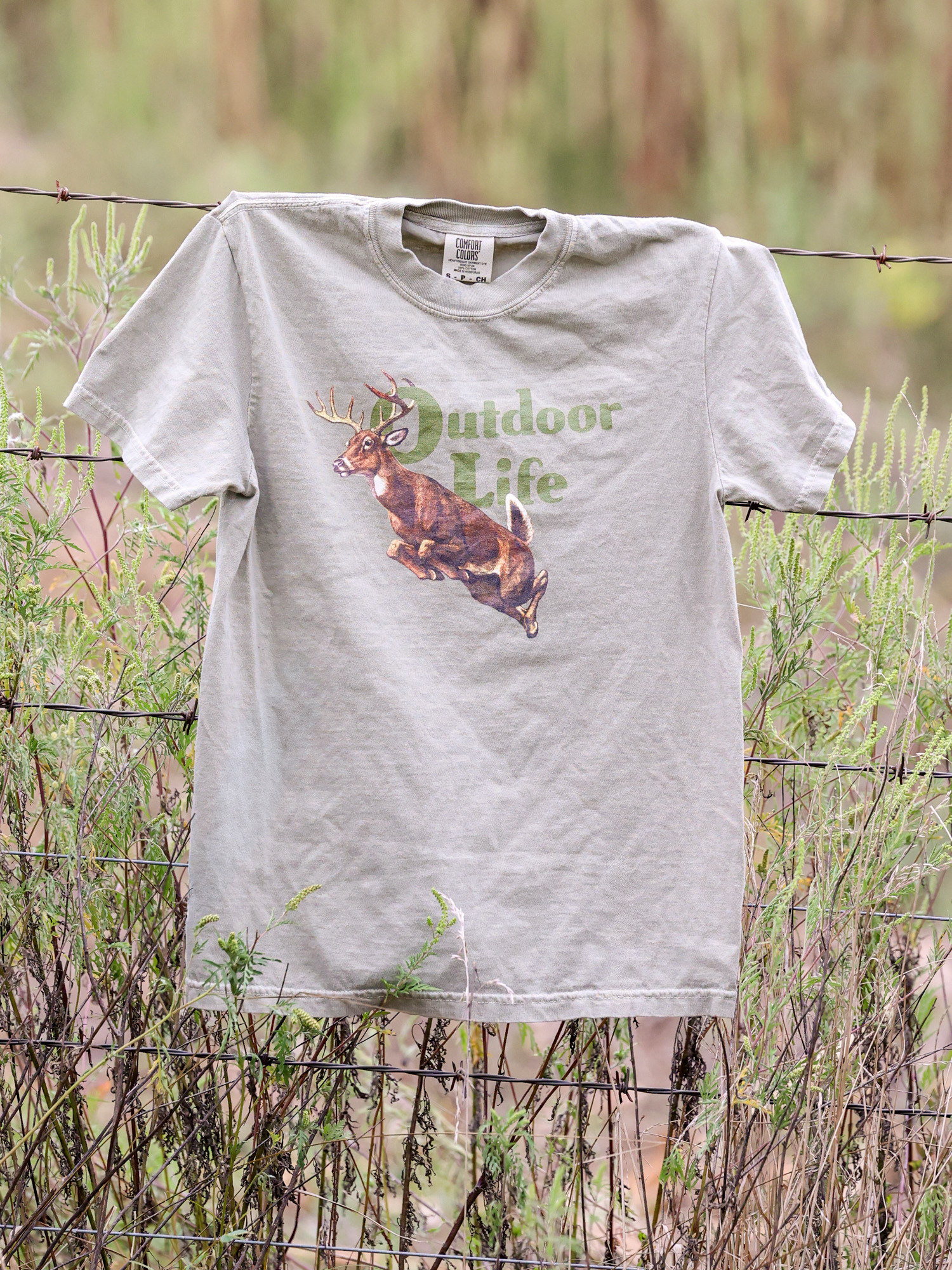 An Outdoor Life big buck khaki colored t-shirt on a barbed wire fence