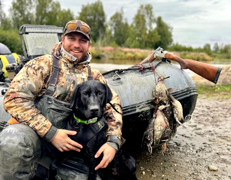 A hunter smiles alongside his bird dog after a successful duck hunt.