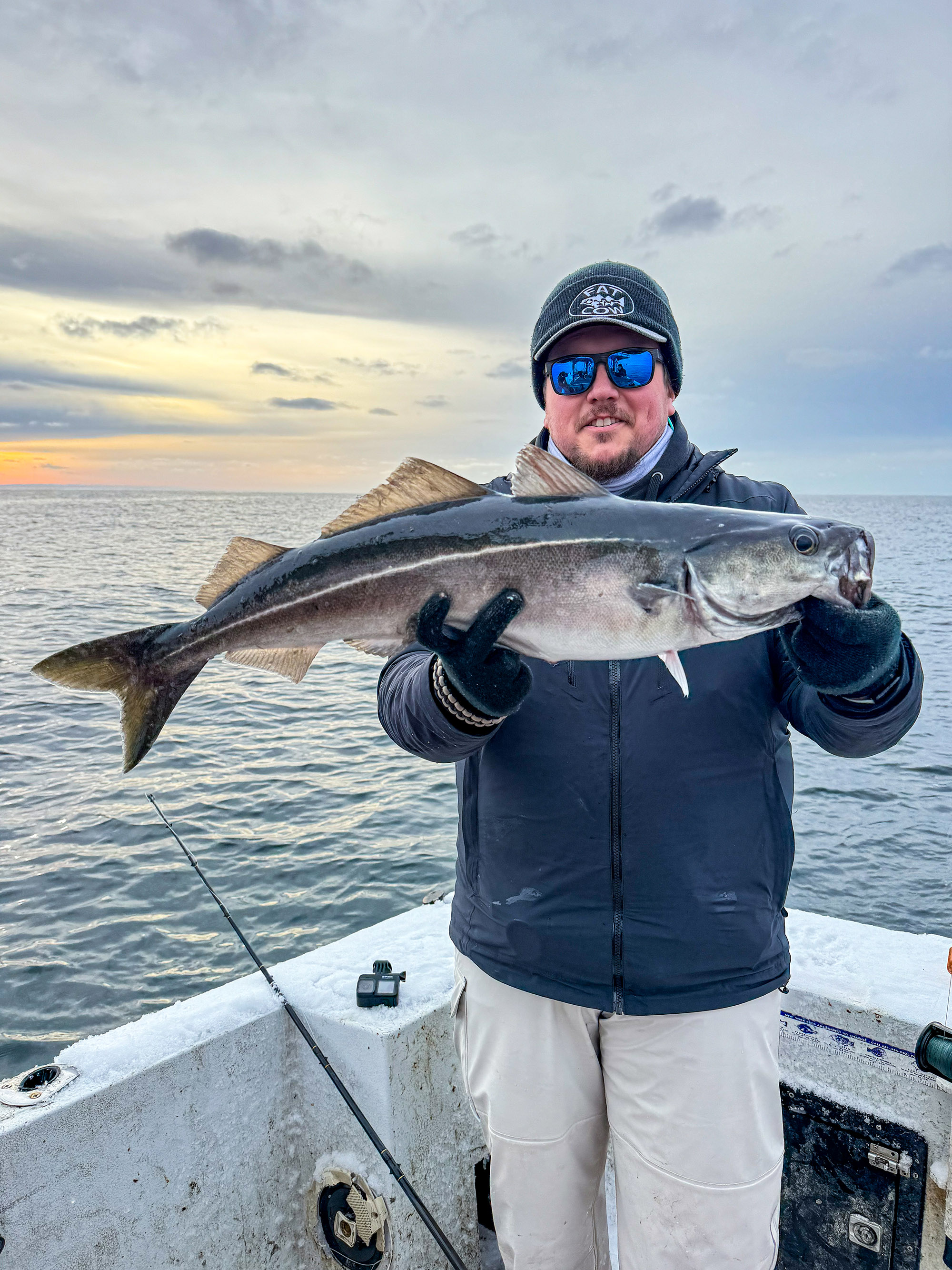 A fisherman stands at the corner of a boat and holds up a winter pollcok.