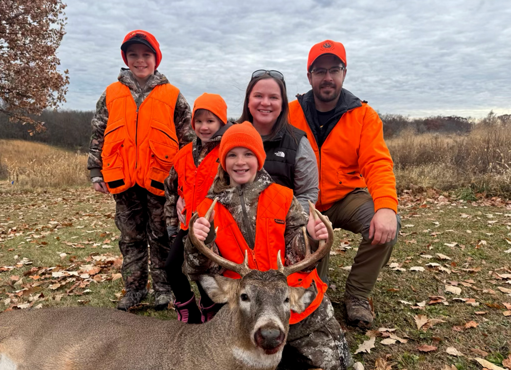A family kneels with their daughter alongside her first buck.