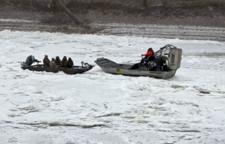 A crew in an airboat comes to the aid of a boat locked in river ice.